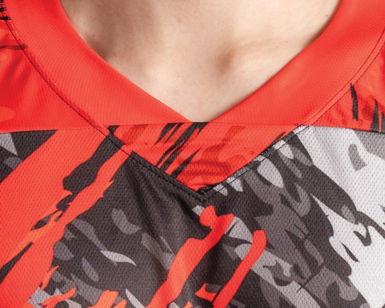 May include: Close-up of a red and black athletic jersey with a v-neck collar. The jersey has a camouflage pattern with red and black accents.