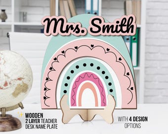 May include: A wooden desk name plate for a teacher, with a rainbow design and the name "Mrs. Smith" in black script. The rainbow has layers of pink, blue, and white, with heart and dot details. The text "WOODEN 2 LAYER TEACHER DESK NAME PLATE" is also visible.