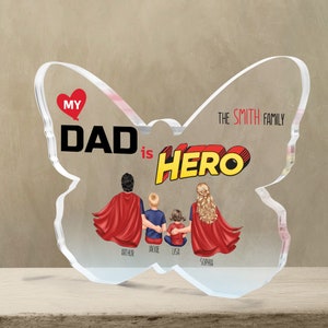 K&ouml;nnte beinhalten: Ein transparentes Acryl-Andenken in Form eines Schmetterlings mit dem Text "My Dad is Hero" in roten und gelben Comic-Buchstaben. Der Schmetterling hat ein rotes Herz mit dem Wort "My" darin. Der Text "The Smith Family" ist auf dem rechten Fl&uuml;gel gedruckt. Vier Figuren einer Familie sind in der Mitte des Schmetterlings dargestellt, mit den Namen Arthur, Jackie, Lisa und Sophia darunter.
