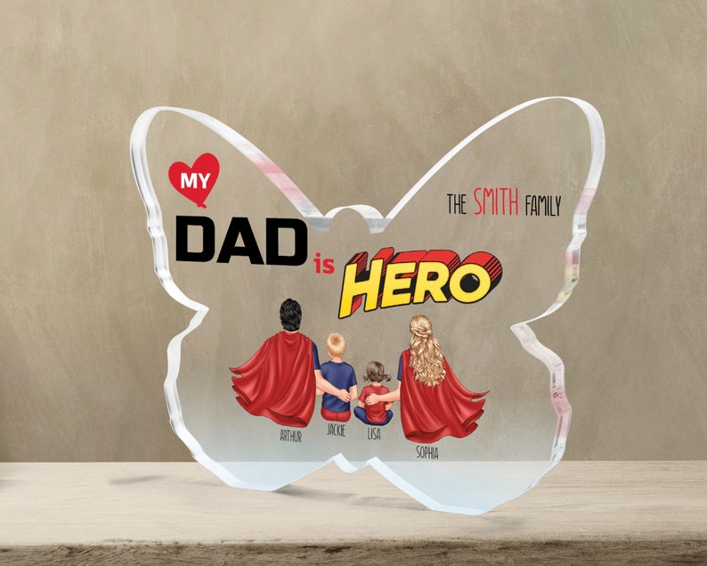 K&ouml;nnte beinhalten: Ein transparentes Acryl-Andenken in Form eines Schmetterlings mit dem Text "My Dad is Hero" in roten und gelben Comic-Buchstaben. Der Schmetterling hat ein rotes Herz mit dem Wort "My" darin. Der Text "The Smith Family" ist auf dem rechten Fl&uuml;gel gedruckt. Vier Figuren einer Familie sind in der Mitte des Schmetterlings dargestellt, mit den Namen Arthur, Jackie, Lisa und Sophia darunter.