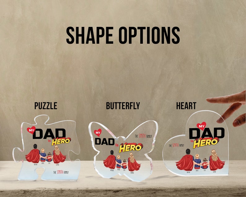 K&ouml;nnte beinhalten: Drei Acrylformen, ein Puzzle, ein Schmetterling und ein Herz, jede mit einem personalisierten Design mit dem Text "Mein Vater ist ein Held" und einer Familienillustration. Die Formen sind klar und haben eine gl&auml;nzende Oberfl&auml;che.