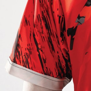 May include: Red and black patterned short-sleeved shirt with a white trim around the sleeve.