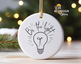 May include: White ceramic ornament with a black lightbulb and the text "Be the light" in a handwritten font.