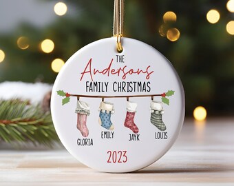 May include: White ceramic Christmas ornament with the text "The Andersons Family Christmas" and four stockings hanging from a branch. The stockings are labeled "Gloria", "Emily", "Jayk", and "Louis". The year 2023 is printed at the bottom.