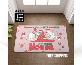 May include: A pink rectangular doormat with a festive design. The mat features a snowman, Santa Claus, and a polar bear illustration. Text reads "There's Some Ho's Ho's Ho's In This House". Decorative flowers and stars surround the text and characters.