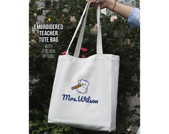May include: White canvas tote bag with long handles, embroidered with a pencil and paper design, and the name "Mrs. Wilson" in blue script. The bag also features the text "Embroidered Teacher Tote Bag with 8 Design Options."