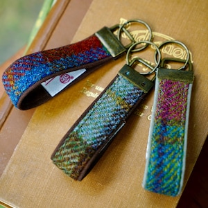 May include: Three fabric keychains featuring a herringbone pattern in vibrant shades of blue, green, red, and purple. Each keychain is attached to a bronze-toned metal split ring and a rectangular metal clasp, with a small white fabric tag visible.