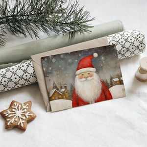 May include: A Christmas card with a watercolor illustration of Santa Claus in a red suit with a white beard and a snowy village in the background. The card is in a brown envelope with a green and white patterned wrapping paper.