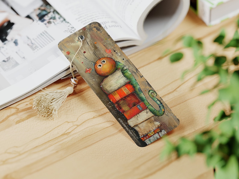 May include: A colorful bookmark featuring a cartoon caterpillar with large eyes, perched on top of a stack of books. The caterpillar is green with a brown head and has a whimsical, cartoonish style.