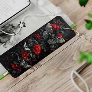 May include: A black bookmark with a dark floral design featuring red roses and white butterflies. The bookmark has a gold tassel.
