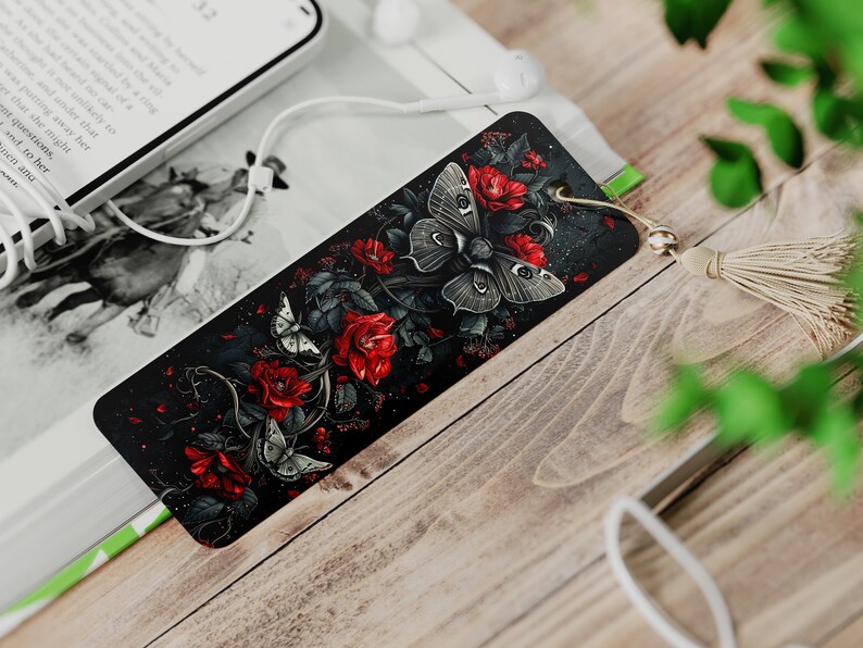 May include: A black bookmark with a dark floral design featuring red roses and white butterflies. The bookmark has a gold tassel.