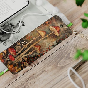 May include: A bookmark featuring a watercolor painting of red and yellow mushrooms with brown stems on a dark background. The bookmark has a beige tassel.