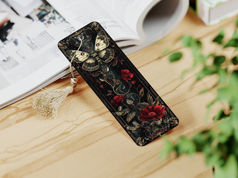 May include: A black bookmark with a gold and white butterfly design and red flowers. The bookmark has a tassel.