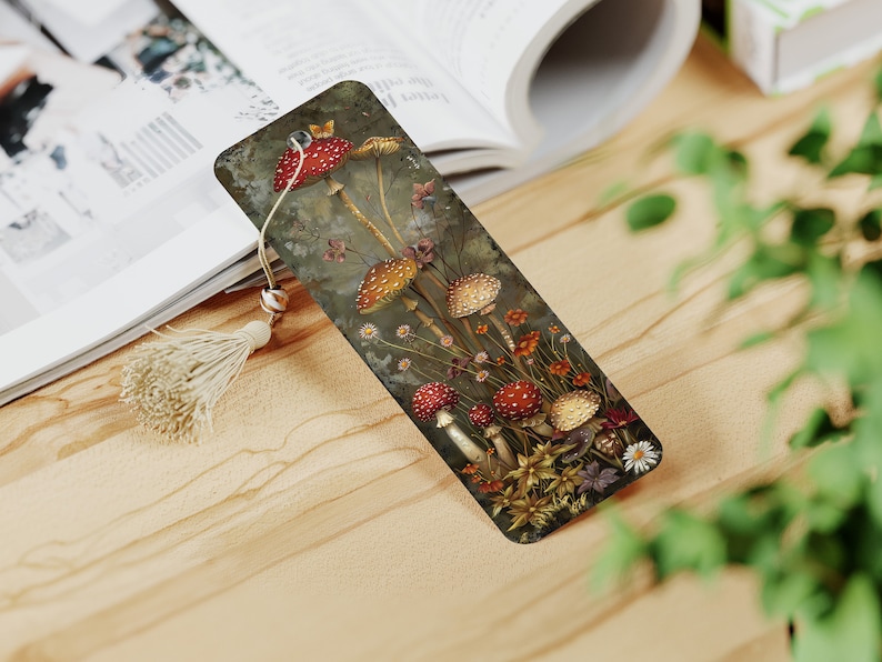 May include: A bookmark featuring a detailed illustration of red and white mushrooms with yellow stems growing in a forest setting. The bookmark is made of a dark brown material and has a tassel.