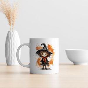 May include: White ceramic mug with a watercolor illustration of a young witch wearing a black hat and orange bow. The witch is standing on a background of orange and brown watercolor splatters.