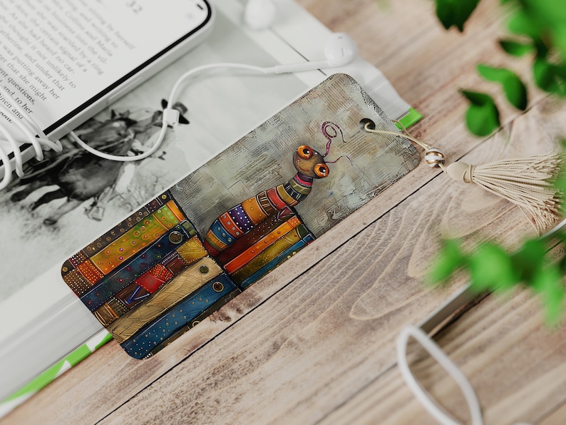 May include: A colorful bookmark featuring a cartoon bug with large eyes standing on a stack of colorful books. The bookmark has a tassel attached to it.