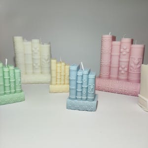 Pode incluir: Conjunto de cinco velas em forma de livro em várias cores, incluindo verde, amarelo, azul e rosa. Cada vela apresenta um design detalhado de livros empilhados com detalhes decorativos.