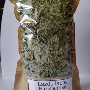 May include: A brown paper bag with a clear plastic window, filled with dried green hazelnut leaves. The bag has a white label that reads "Lazdu lapas Hazelnut leaf corylus avellana 60g".