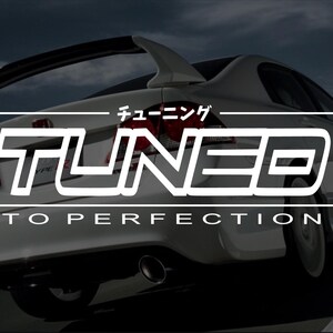May include: White sports car with a spoiler, featuring the word "TUNED" in bold white letters, with Japanese characters above and "TO PERFECTION" below. The car is set against a dark, blurred background.