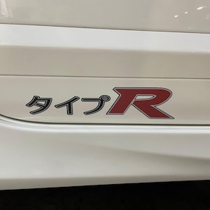 May include: A white vehicle side panel with a black and red "TYPE R" emblem. The emblem features Japanese characters and a bold red "R" in a stylized font, indicating a performance model.