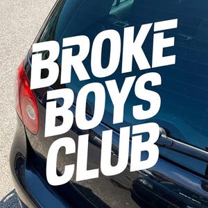 Puede incluir: La ventana trasera de un coche azul oscuro muestra una calcomanía blanca con el texto "BROKE BOYS CLUB" en una fuente en negrita. La luz trasera y el limpiaparabrisas del coche son visibles.