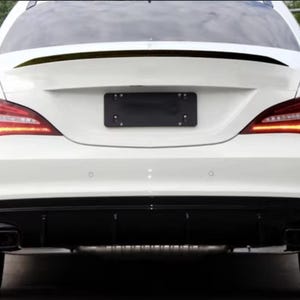 May include: Rear view of a white car with black accents. The car features sleek taillights, a black rear diffuser, and dual exhaust pipes. A black license plate is centered above the diffuser.