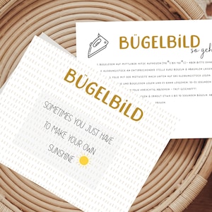 Könnte beinhalten: Eine weiße Karte mit schwarzem und goldenem Text. Die Karte enthält Anweisungen zum Aufbügeln eines Bügelbildes. Der Text lautet "Bügelbild so geht's" und enthält Anweisungen auf Deutsch. Die Karte enthält auch den Text "Sometimes you just have to make your own sunshine" mit einem gelben Sonnensymbol.