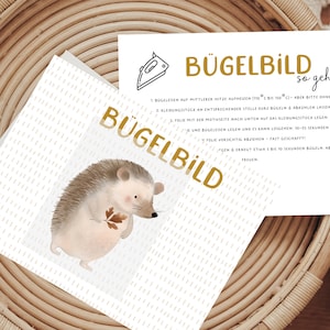 Könnte beinhalten: Eine weiße Karte mit goldener Schrift, auf der "Bügelbild so geht's" steht und Anweisungen zum Aufbügeln eines Bildes. Die Karte zeigt eine niedliche Illustration eines Igels, der ein Blatt hält.