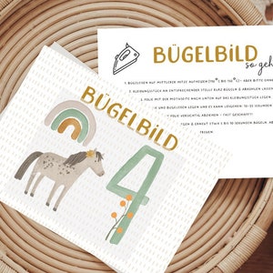 Könnte beinhalten: Eine weiße Karte mit einer grünen Zahl Vier und einer Illustration eines braunen und weißen Pferdes. Die Karte hat auch einen Regenbogen und den Text "Bügelbild" in goldenen Buchstaben. Eine separate weiße Karte mit Anweisungen zum Aufbügeln eines Bügelbildes ist ebenfalls abgebildet. Der Text auf der Karte lautet "Bügelbild so geht's".
