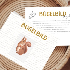 Könnte beinhalten: Eine weiße Karte mit dem Text "Bügelbild so geht's" in goldenen Buchstaben. Die Karte enthält Anweisungen, wie man ein Design aufbügelt. Die Karte liegt auf einem geflochtenen Korb mit einer braunen Eichhörnchen-Illustration.