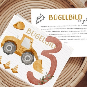 Könnte beinhalten: Ein gelbes und graues Spielzeug-Baufahrzeug mit Schaufel, einer Nummer drei und drei orangefarbenen Verkehrskegeln. Das Bild enthält Anweisungen zum Aufbügeln eines Bügelbildes auf Stoff.