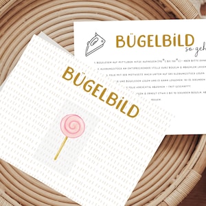 Könnte beinhalten: Eine weiße Karte mit goldener Schrift, auf der "Bügelbild" steht und Anweisungen zum Aufbügeln eines Bildes. Die Karte liegt in einem geflochtenen Korb.