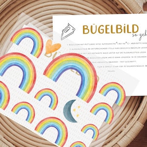 Könnte beinhalten: Ein Bogen mit Bügelbildern, der mehrere regenbogenfarbene Motive im Aquarellstil in verschiedenen Größen, ein kleines orangefarbenes Herz, eine dunkelblaue Mondsichel und drei gelbe Sterne zeigt, inklusive einer Anleitungskarte mit der Überschrift BÜGELBILD so geht's.