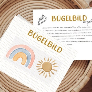 Könnte beinhalten: Eine weiße Karte mit Anweisungen zum Aufbügeln eines Bügelbildes. Die Karte zeigt ein Regenbogen- und Sonnenmotiv und den Text "Bügelbild so geht's".
