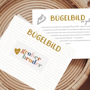 Könnte beinhalten: Eine weiße Karte mit dem Text "Bügelbild so geht's" und Anweisungen zum Aufbügeln eines Stickers. Die Karte liegt in einem geflochtenen Korb mit einer kleineren weißen Karte, auf der "Bügelbild" in goldenen Buchstaben und "großer Bruder" in bunten Buchstaben steht.