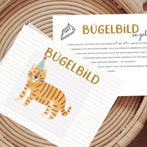 Könnte beinhalten: Eine weiße Karte mit einem Tiger, der einen Partyhut trägt, und dem Text "Bügelbild so geht's" in goldenen Buchstaben. Die Karte enthält Anweisungen zur Verwendung von Bügelbildern.