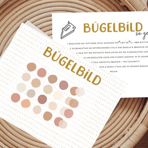 Könnte beinhalten: Zwei Karten mit dem Text "BÜGELBILD" und Bügelanweisungen. Eine Karte zeigt ein Muster aus neutralfarbenen Kreisen. Die Karten liegen auf einer gewebten Oberfläche.