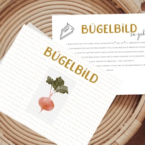 Könnte beinhalten: Eine weiße Karte mit dem Text "Bügelbild so geht's" in schwarzer und goldener Schrift. Die Karte enthält Anweisungen zum Aufbügeln eines Bügelbildes. Die Karte liegt auf einem geflochtenen Korb mit weißem Hintergrund.
