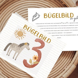 Könnte beinhalten: Eine weiße Karte mit einer braunen Zahl drei und einer gelben Sonne. Die Karte hat auch ein graues Pferd mit einer braunen Mähne und einem braunen Schwanz. Der Text auf der Karte lautet "Bügelbild 3" und "Bügelbild so geht's".