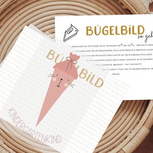 Könnte beinhalten: Zwei Karten mit Text und Illustrationen werden in einem Weidenkorb angezeigt. Eine Karte zeigt eine rosa Eiswaffel-Grafik mit den Worten "Kindergartenkind". Die andere Karte enthält Anweisungen auf Deutsch.