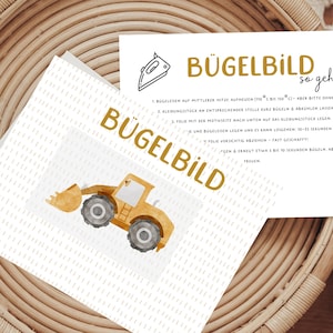 Könnte beinhalten: Ein Bügelbild mit einem gelben Bauwagen-Motiv auf einer weißen Karte mit goldfarbenem Schriftzug "BÜGELBILD". Eine separate Karte enthält Anweisungen. Das Bild liegt auf einer gewebten, kreisförmigen, hellbraunen Oberfläche.