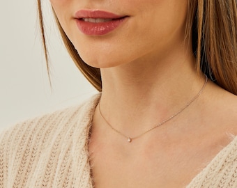 Puede incluir: Un delicado collar de cadena de oro con un pequeño colgante redondo de piedra preciosa transparente.