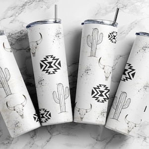 Op de afbeelding: Vier witte geïsoleerde bekers met zwart-witte Southwestern-ontwerpen. Elke beker heeft een ander ontwerp, waaronder een cactus, een schedel van een stier en geometrische patronen. De bekers hebben zilveren rietjes en zwarte spikkels.