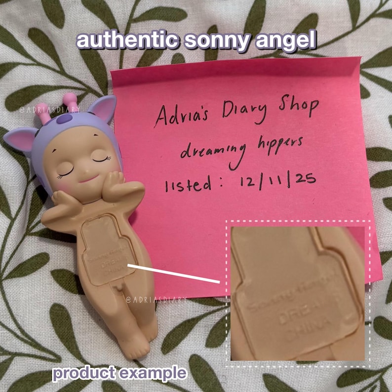 K&ouml;nnte beinhalten: Beige Sonny Angel Figur mit lavendelfarbenem Hut und geschlossenen Augen, die ihr Kinn auf ihren H&auml;nden ruhen l&auml;sst. Ein pinkfarbener Haftzettel mit der Aufschrift "Adria's Diary Shop dreaming hippers listed: 12/11/25". Die Texte "authentic sonny angel" und "product example" sind ebenfalls sichtbar.
