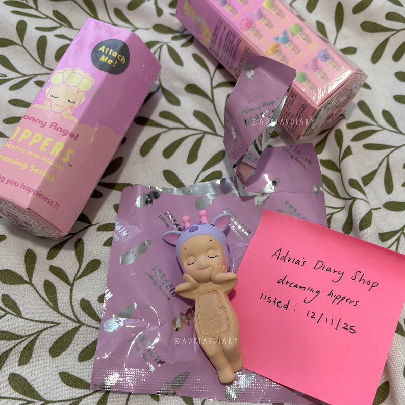 K&ouml;nnte beinhalten: Eine Sammlung von Sonny Angel Dreamy Hippers Figuren, darunter eine Figur im Giraffen-Design, Verpackungen und ein pinkfarbener Haftzettel mit handschriftlichem Text. Die Schachteln und Verpackungen sind haupts&auml;chlich rosa und lila.
