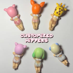 Puede incluir: Seis figuras personalizadas con cabezas tem&aacute;ticas de animales y trajes de ba&ntilde;o. Las figuras tienen cabezas rosas, naranjas y amarillas con rasgos de animales. El texto "CUSTOMIZED HIPPERS" se muestra en el centro de la imagen.