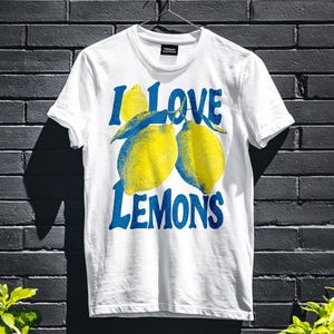 I Love Lemons t-shirt design featuring three hand-drawn yellow lemons with blue shading and bold retro blue text that says “I LOVE LEMONS.” A vibrant summer fruit graphic perfect for sublimation, printable t-shirts, summer merch, lemon-themed gifts, or wall art. Includes high-resolution PNG and PDF files for instant download. Ideal for fruit lovers, bold fashion, and sunny summer apparel.