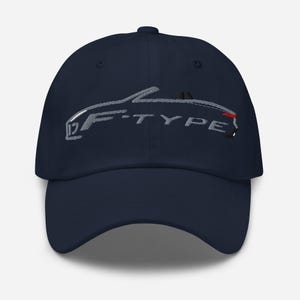 Puede incluir: Gorra de béisbol azul marino con contorno plateado bordado de un coche y el texto "F-TYPE". La gorra tiene una visera curva y un botón. Un accesorio elegante para los entusiastas de los coches.