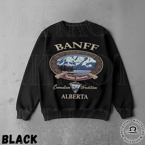 May include: Black sweatshirt with a Banff, Alberta design. The design features an oval image of mountains and a lake, with text that reads "Outdoor Discovery" and "Canadian Tradition". The word "Banff" is arched across the top.