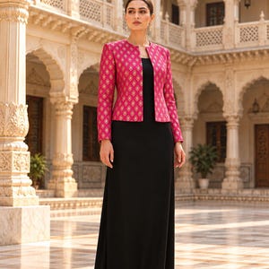 May include: A long black floor-length dress paired with a vibrant fuchsia jacket featuring a repeating gold diamond pattern. The jacket has long sleeves, a round neckline, and an open front, while the dress is sleeveless with a simple silhouette.